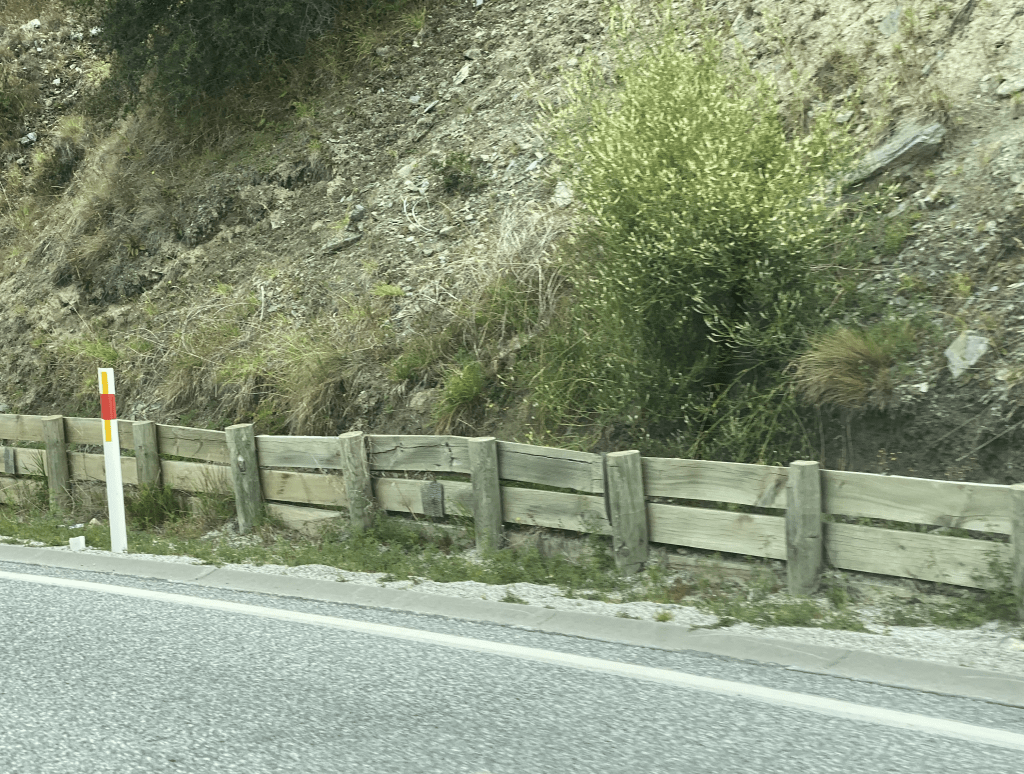 Road side picture showing paved road, reflective pole, road marking, 50cm wooden rock protection wall